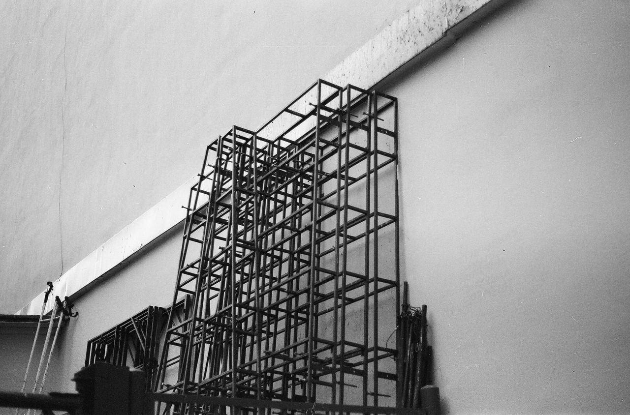 Black and white photo of a metal structure against a minimalist wall, showcasing modern architecture.
