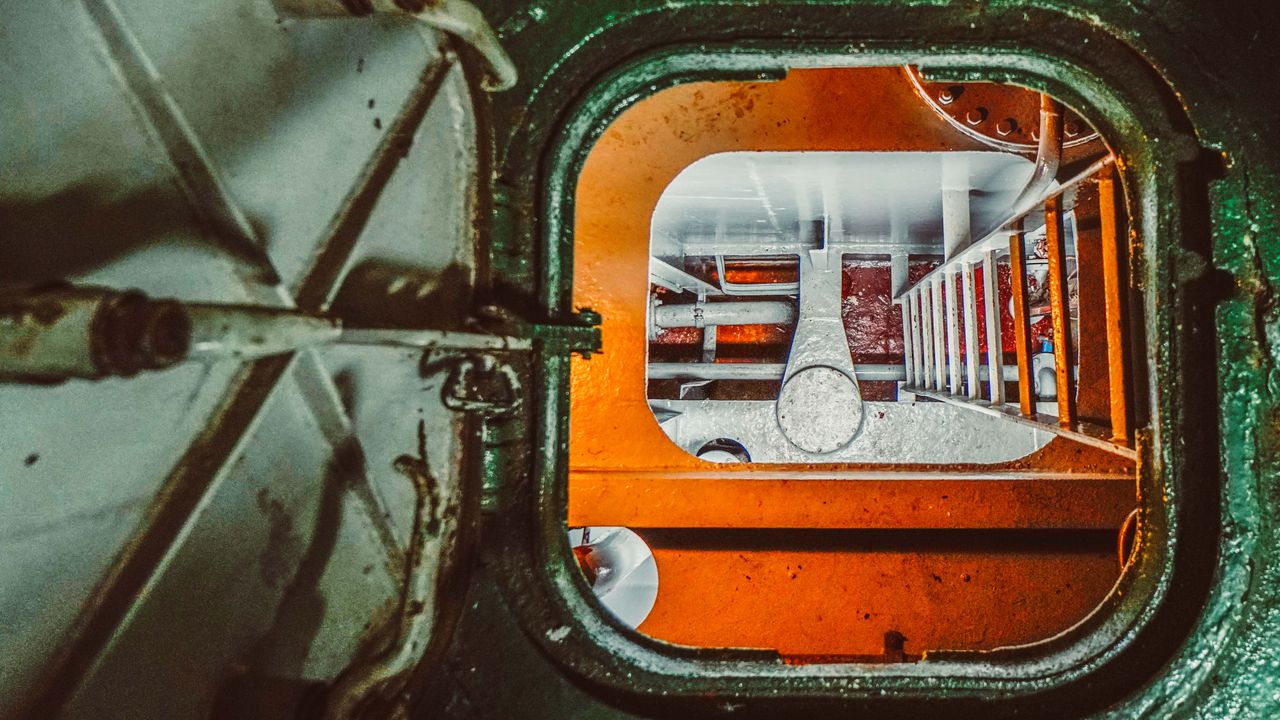 Top view of industrial hatchway with rusty pipes and ladder, showcasing metal structure.